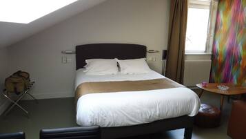 A hotel room with a bed, a chair, a small table, and a window with curtains.