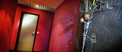 A hallway with a red wall, a door, and a wall-mounted artwork featuring a plant and text.