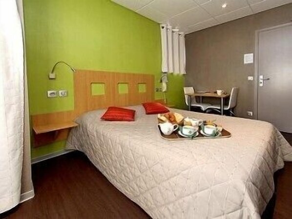 A hotel room with a bed, a small desk, and a chair. There is a tray with cups and a plate on the bed. - Hôtel des Gorges du Tarn (Florac)