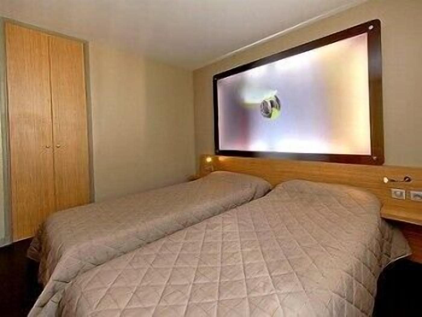 A hotel room with two beds, a wooden wardrobe, and a television mounted on the wall.