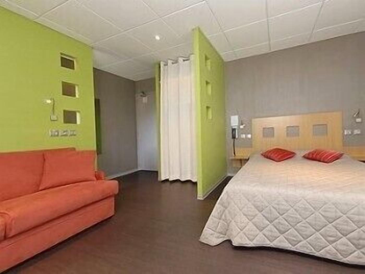A hotel room with a bed, a sofa, and a green accent wall.