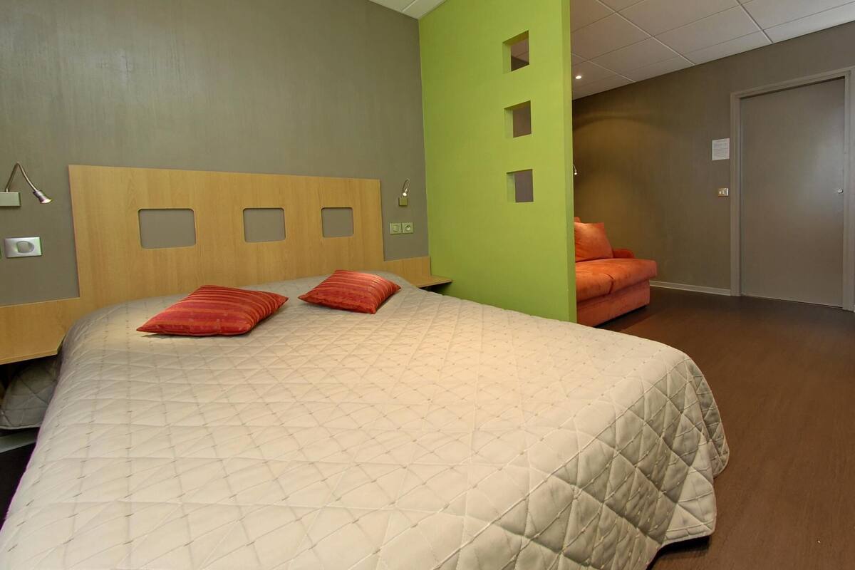 A bedroom with a bed, a chair, a door, and a wall with a green panel.