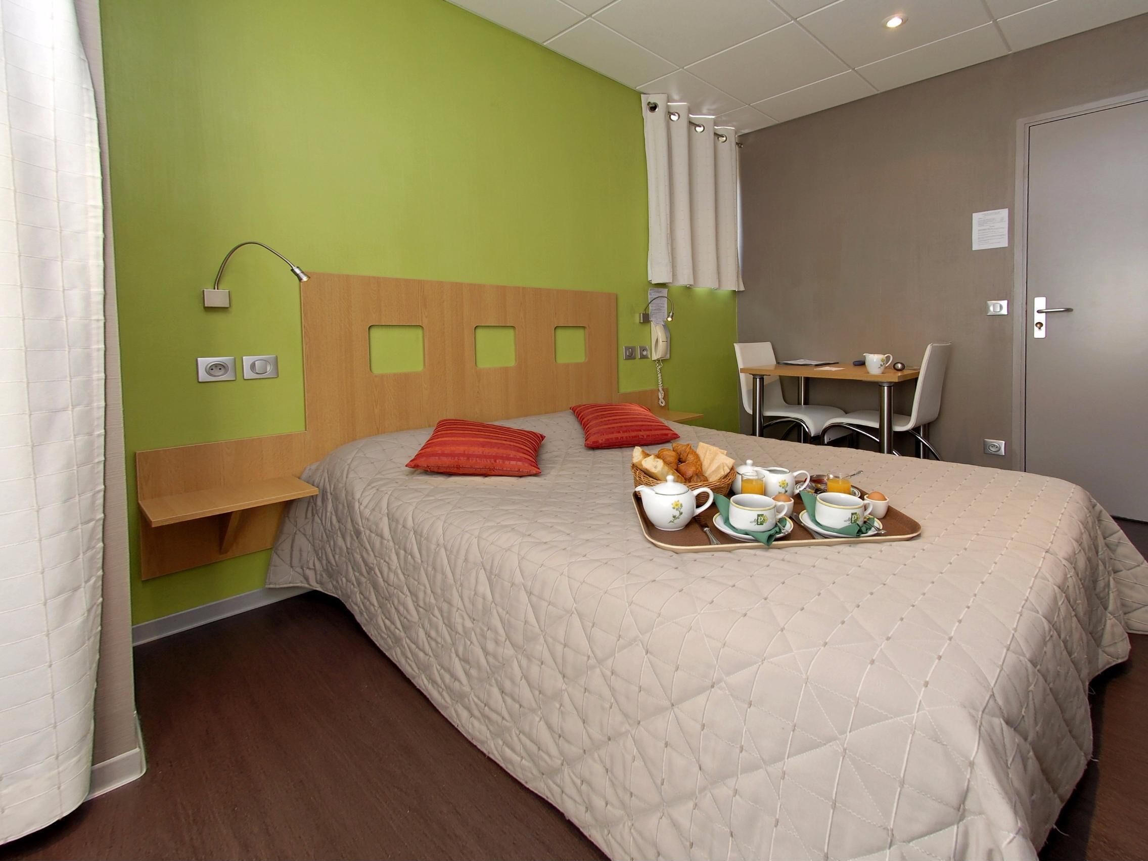 Een hotelkamer met een bed, een ontbijttafel, nachtkastje, bureau, stoel en een telefoon.
