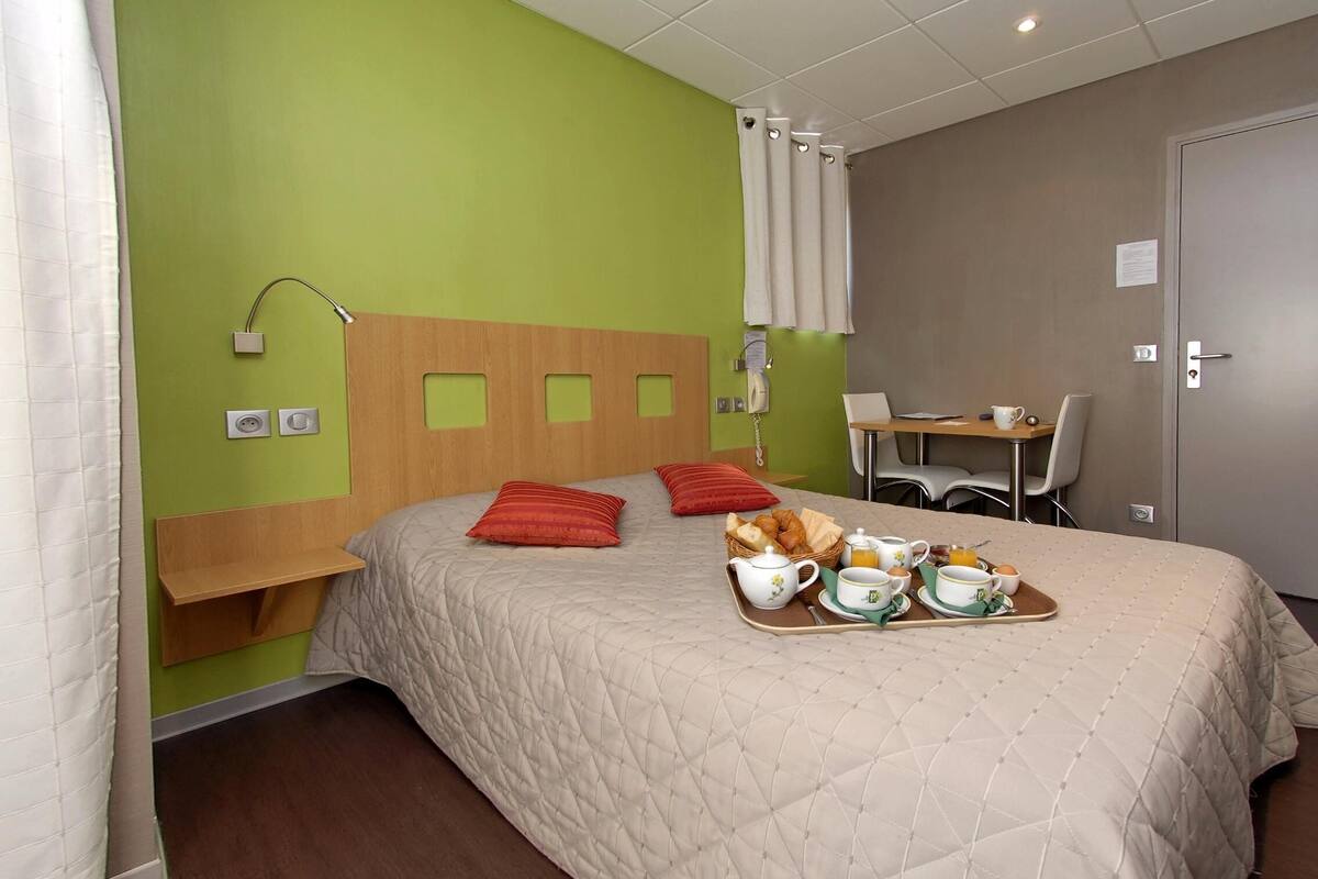 A hotel room with a bed, breakfast tray, bedside table, desk, chair, and a telephone.