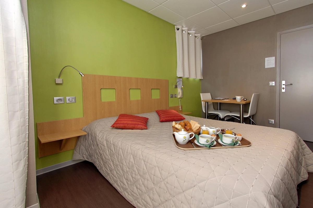 Habitación de hotel con cama, bandeja de desayuno, mesita de noche, escritorio, silla y teléfono.