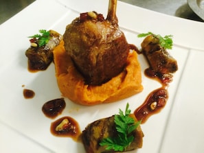 A dish with a lamb shank on a bed of mashed potatoes, garnished with parsley and surrounded by sauce. - Logis Hôtel Au Croissant (Buzancais)