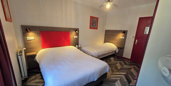 Habitación de hotel con dos camas, una pared de acento roja, una lámpara moderna y un suelo con estampado de espiga.