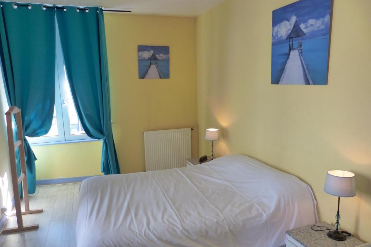 A room with a bed, a nightstand, a lamp, a window with curtains, and two paintings on the wall.