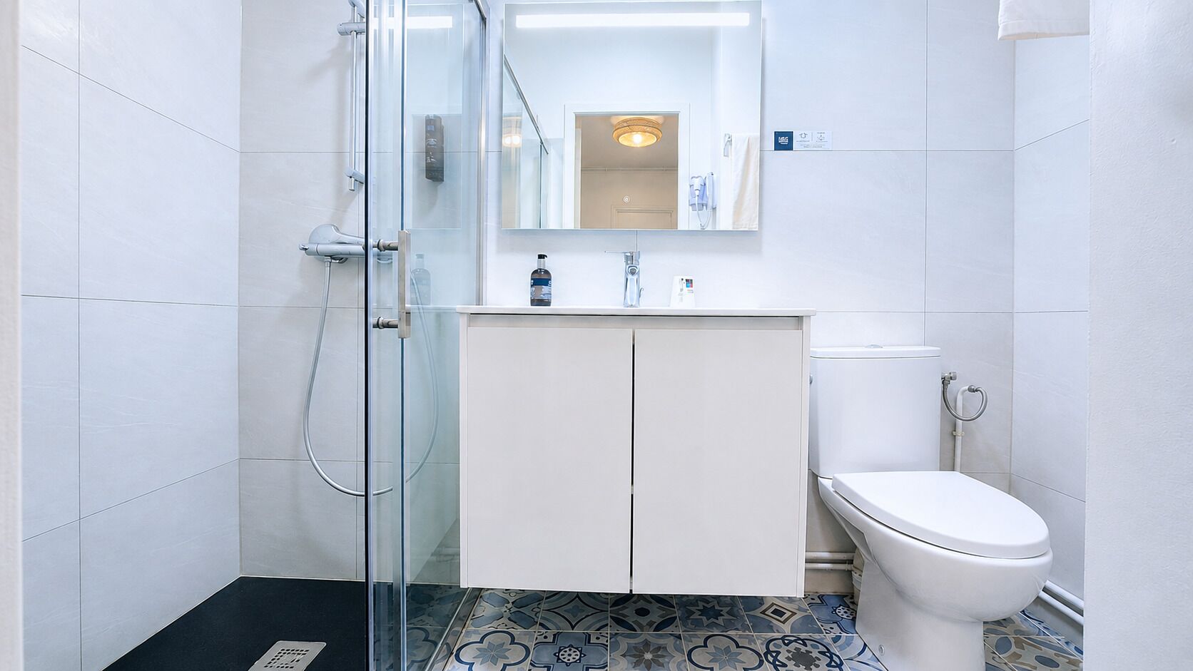 Une salle de bain avec une douche à parois de verre, des toilettes blanches et un meuble avec un miroir au-dessus.
