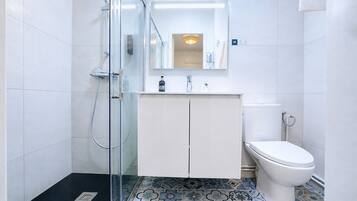 Une salle de bain avec une douche à parois de verre, des toilettes blanches et un meuble avec un miroir au-dessus.