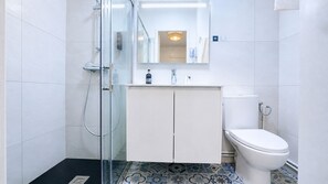 A bathroom with a glass shower enclosure, a white toilet, and a cabinet with a mirror above it.
