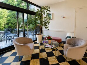 Una habitación con dos sillas, una mesa, una planta en maceta y vistas a un patio exterior con mesas y sillas.