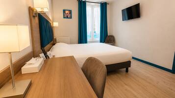 Ein Hotelzimmer mit einem Bett, einem Schreibtisch mit Lampe, einem Sessel, einem Fernseher und einem Fenster mit Vorhängen.