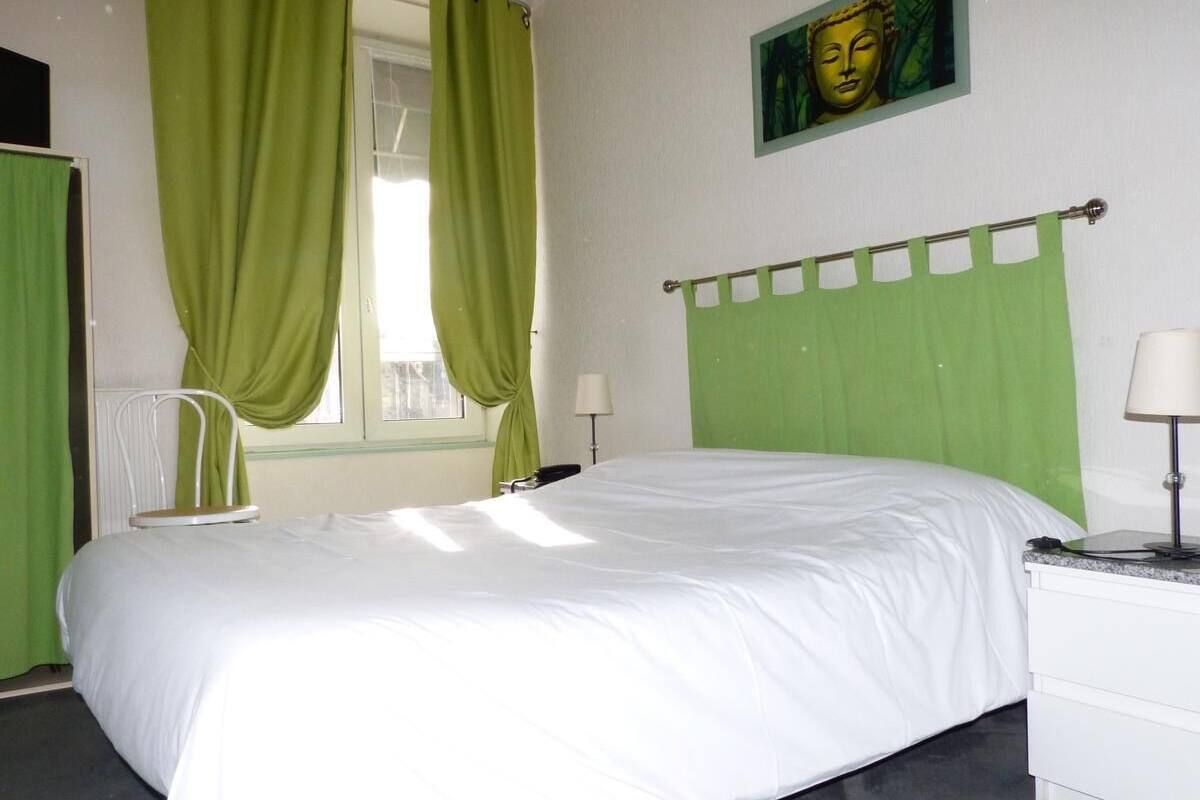 Un dormitorio con cama, una silla, ventana con cortinas, lámpara y un cuadro en la pared.