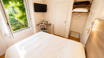 A bedroom with a bed, a chair, a TV, a wardrobe, and a window with a view of greenery.