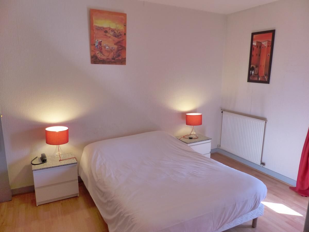 Een slaapkamer met een bed, twee nachtkastjes met lampen, een radiator en twee schilderijen aan de muur.