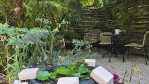 A garden patio with a table and chairs, surrounded by lush greenery and a wooden fence.