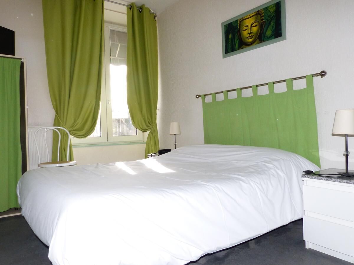 Een slaapkamer met een bed, een stoel, een raam met gordijnen, een lamp en een schilderij aan de muur.