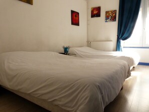 Une chambre avec deux lits, un radiateur et trois tableaux au mur.