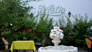 A garden area with a stone fountain, a table with a yellow tablecloth, and chairs. A sign with the word "LeRatti" is visible in the background. - Hôtel du Centre (Molsheim)