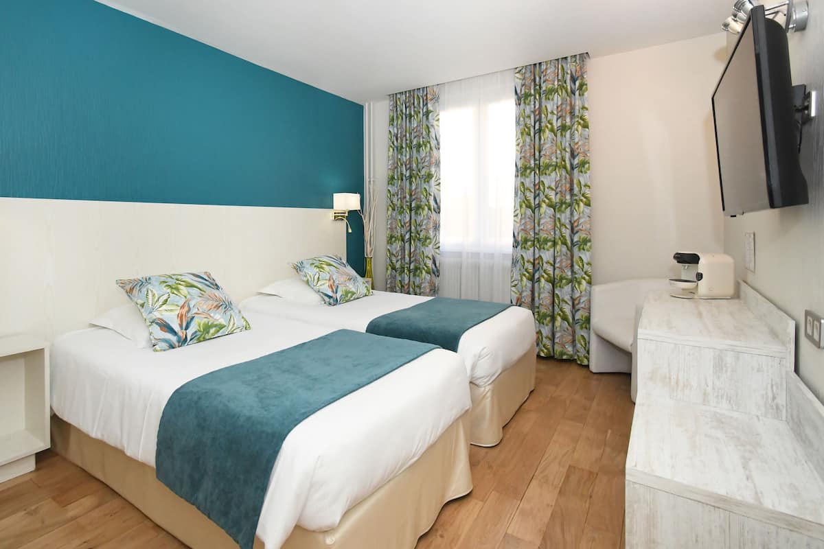 A hotel room with two beds, a TV, a desk, and a window with curtains.