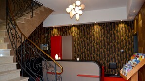 A hotel reception area with a staircase, a reception desk, and a wall with a peacock feather pattern. - Hôtel du Centre (Molsheim)