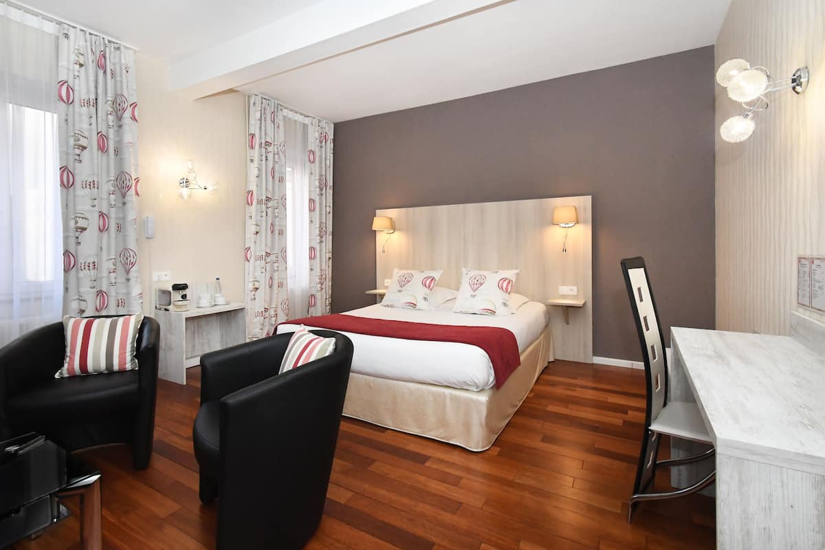 A hotel room with a bed, two chairs, a desk, and a small table.