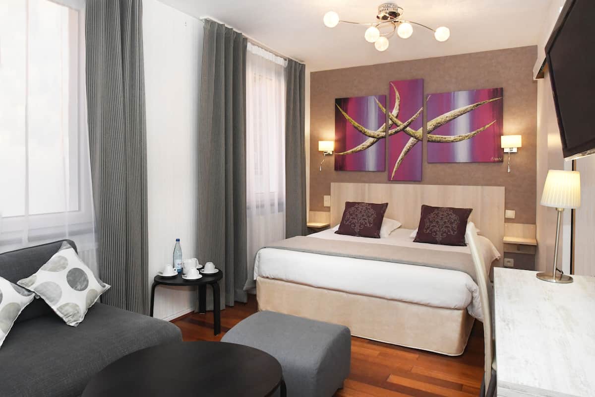 A hotel room with a bed, a sofa, a desk, and a TV.
