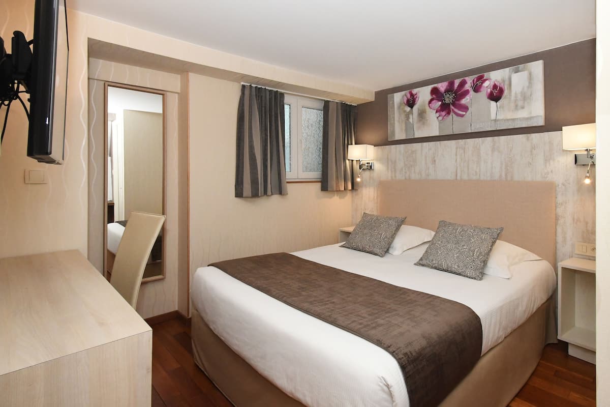 A neatly arranged hotel room with a large bed, bedside lamps, a painting on the wall, and a desk with a chair.