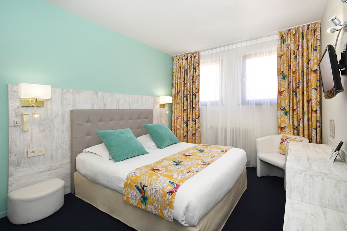 A hotel room with a bed, a bedside table, a chair, and a desk.