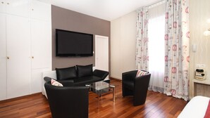 A modern hotel room with a flat-screen TV, a sofa, a chair, and a bed. - Hôtel du Centre (Molsheim)