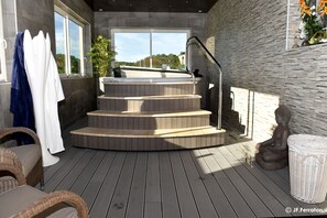 A spa area with a wooden deck, a hot tub, and a statue. - Hôtel Beau Site (Val-d'Arcomie)