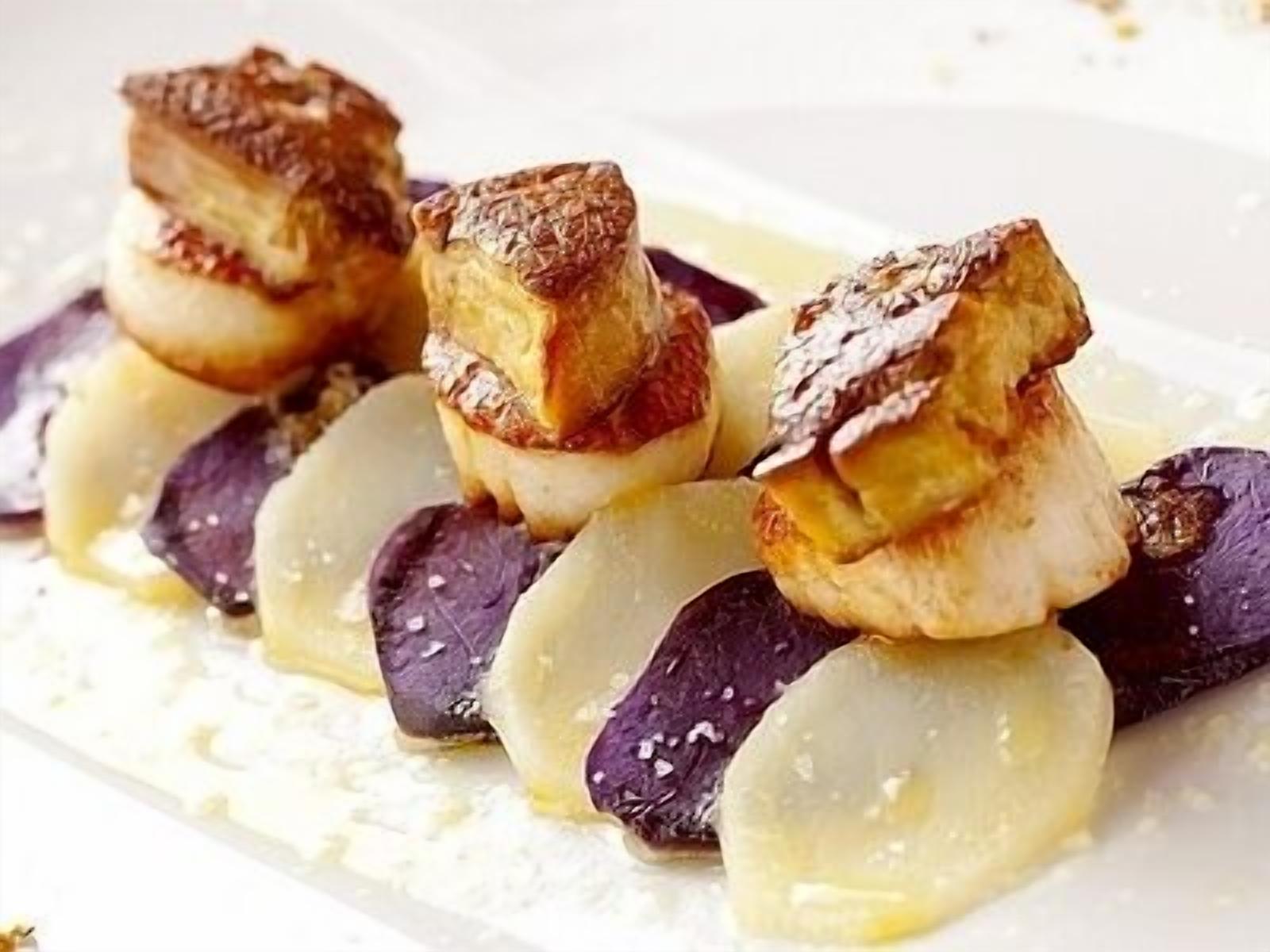 A dessert plate with a pastry, possibly a tart, and slices of purple fruit, likely eggplant, arranged on a white plate.