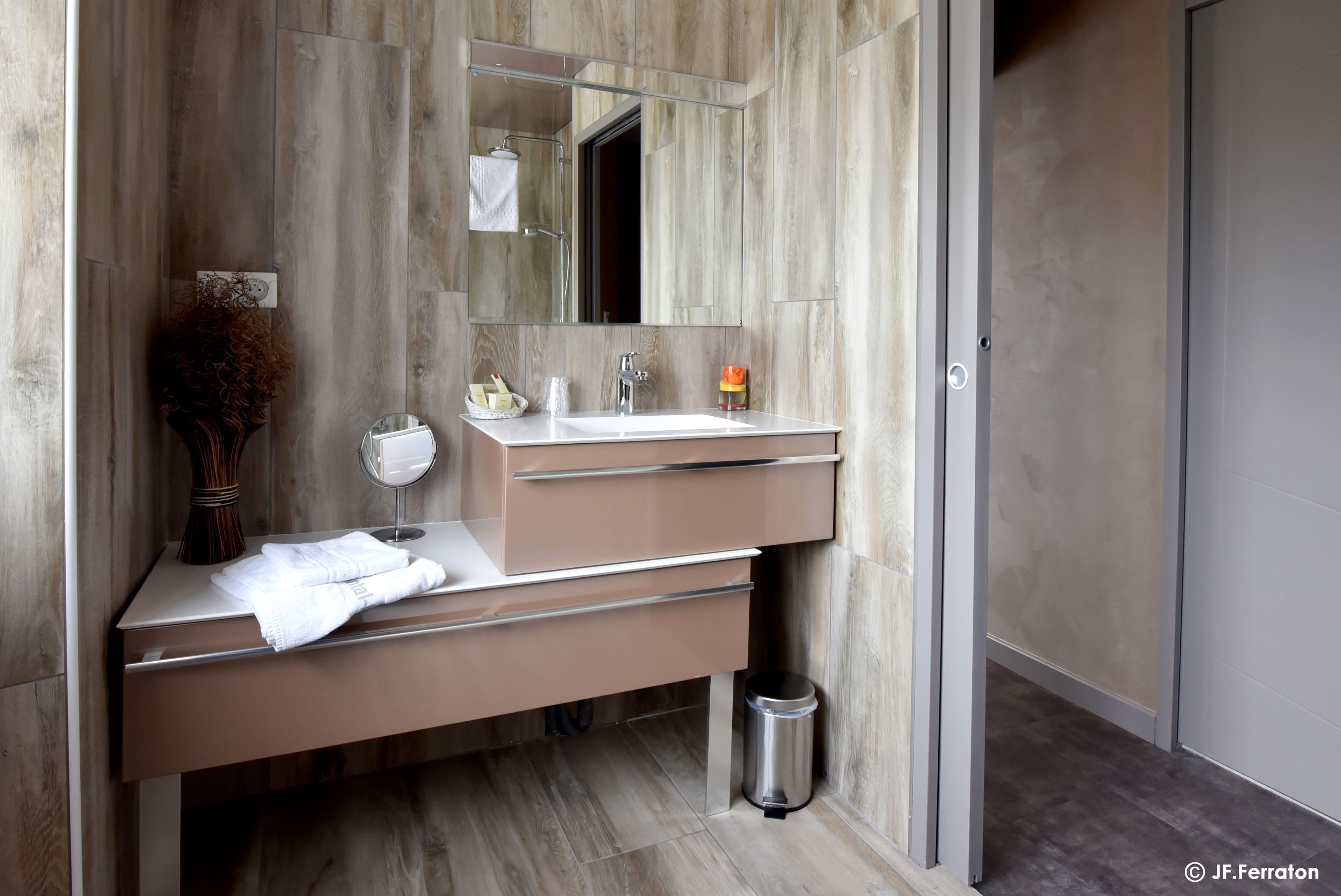Ein modernes Badezimmer mit einem großen Spiegel, einem weißen Waschbecken und einem Waschtisch mit Schubladen.