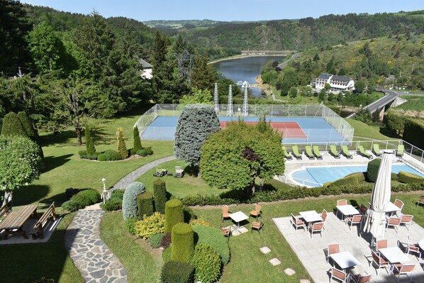 A landscaped outdoor area with a tennis court, seating areas, and a view of a lake and hills.