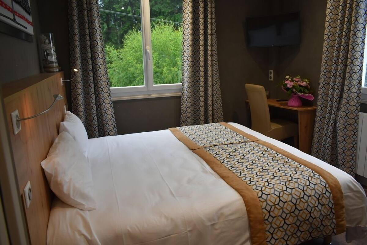 A hotel room with a bed, a desk, a chair, and a TV on the wall.
