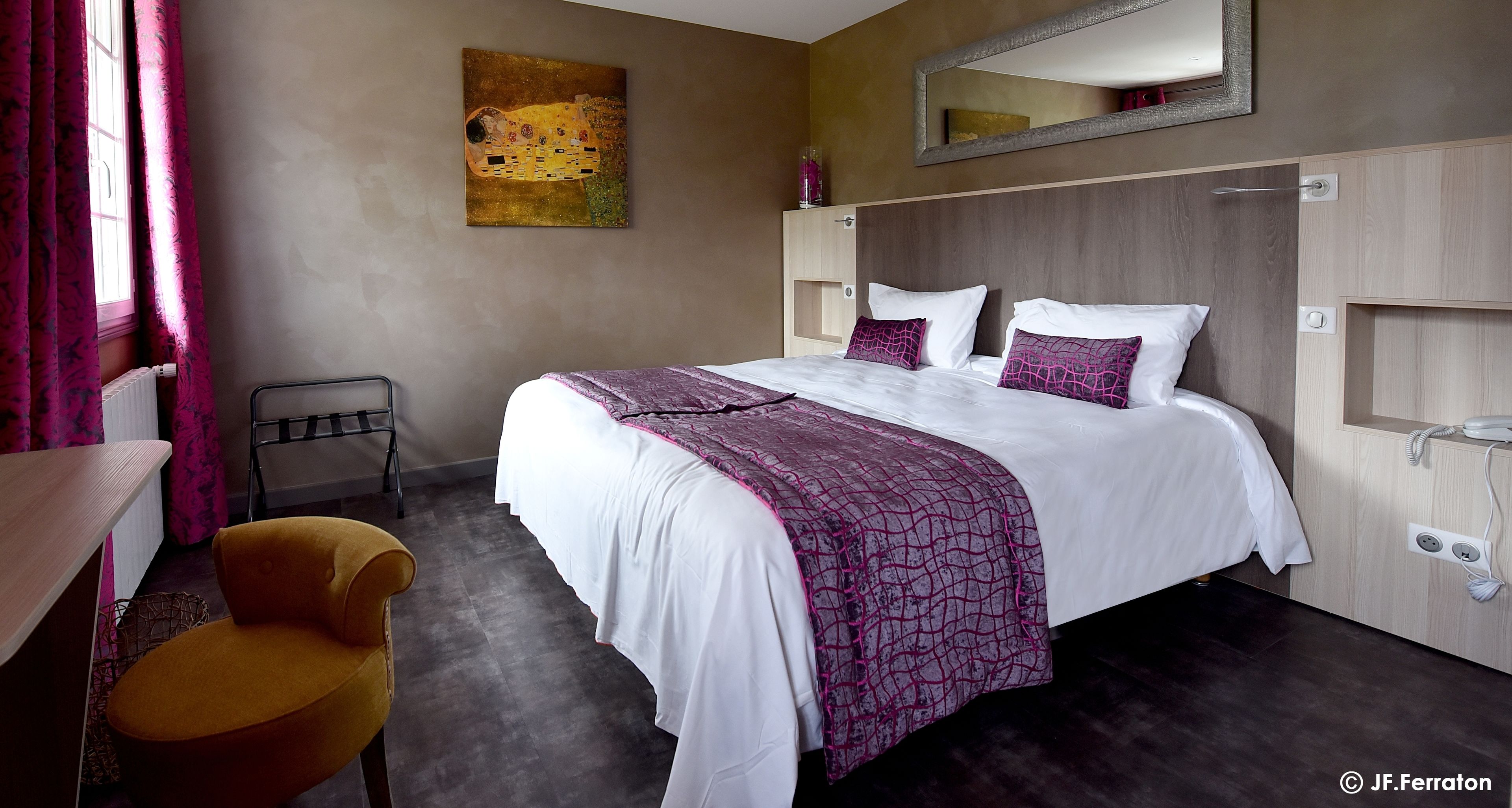 A hotel room with a large bed, a chair, a desk, a mirror, and a painting on the wall.