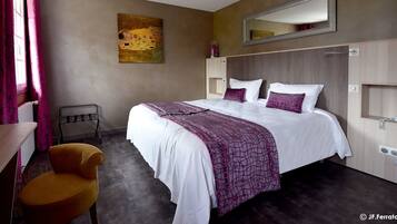 A hotel room with a large bed, a chair, a desk, a mirror, and a painting on the wall.