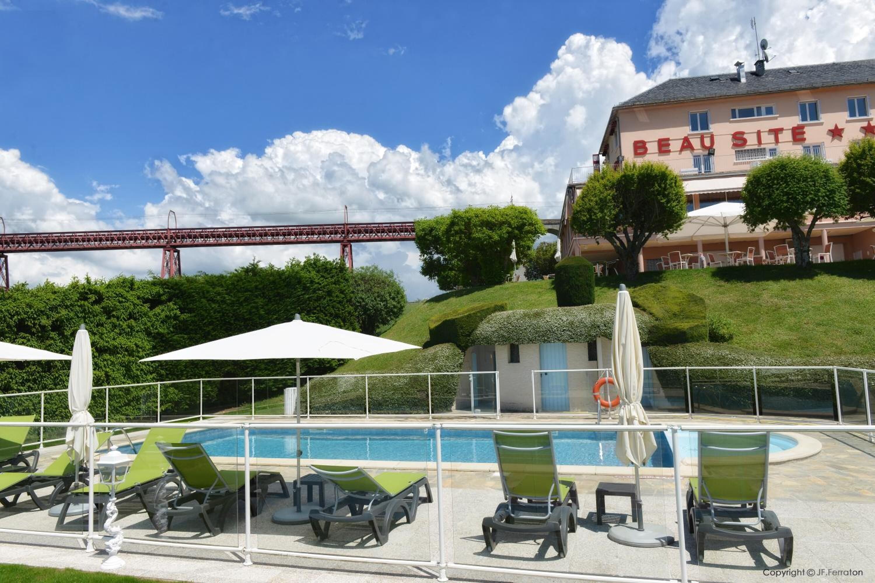 A hotel with a pool area, outdoor seating, and a view of a bridge in the background.