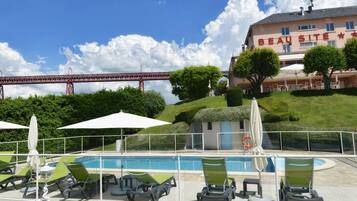 A hotel with a pool area, outdoor seating, and a view of a bridge in the background.