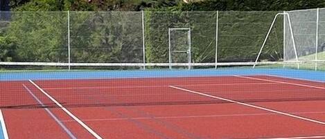 A tennis court with a red surface and white boundary lines.