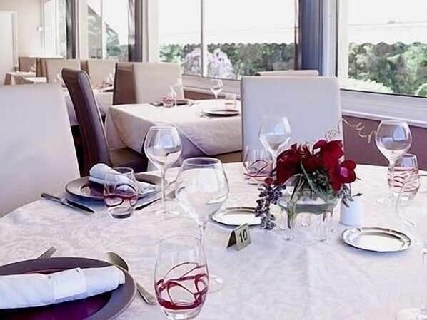 A dining table set with wine glasses, plates, and a vase of red flowers.