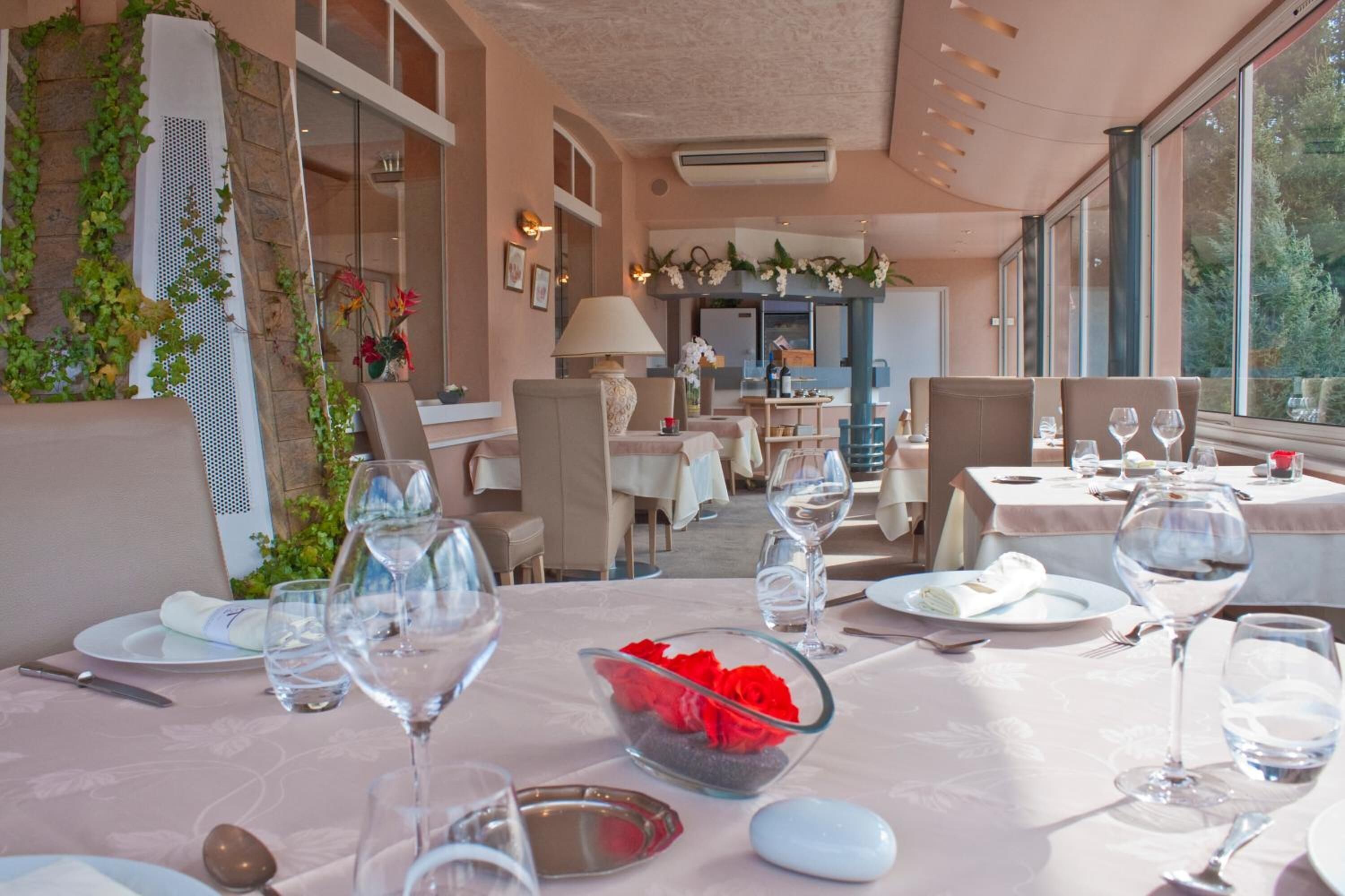 A restaurant with tables set for dining, featuring clear glassware and a bowl of red flowers.