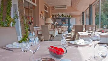 A restaurant with tables set for dining, featuring clear glassware and a bowl of red flowers.