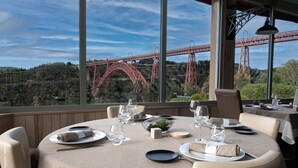 A dining table set for six with a scenic view of a red bridge in the background. - Hôtel Beau Site (Val-d'Arcomie)