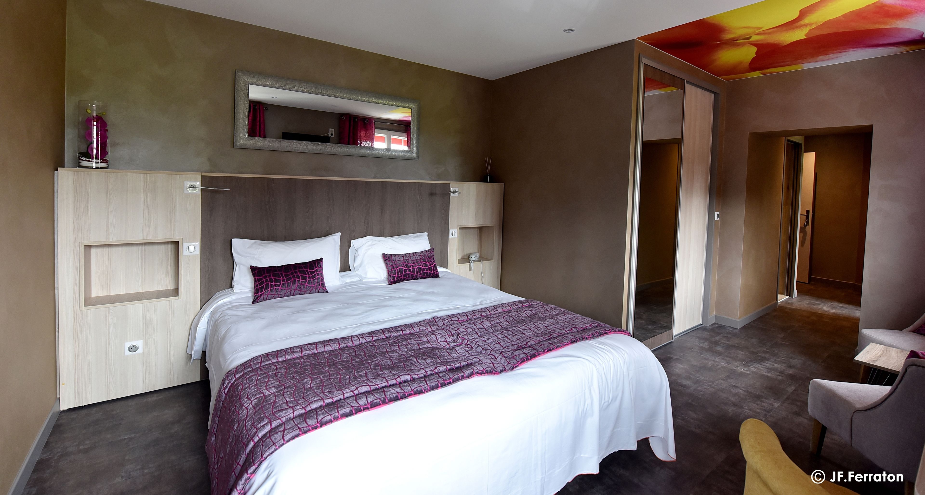 A modern hotel room with a large bed, a bedside table, a mirror, and a door leading to another room.