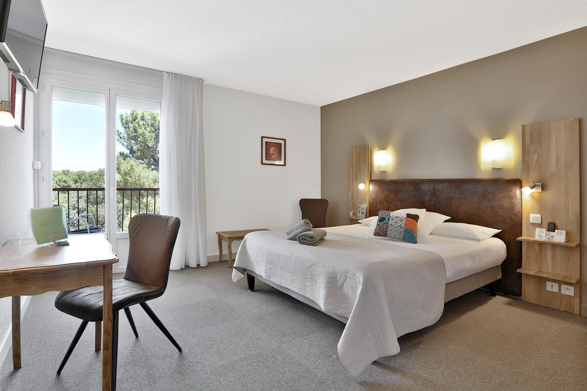 Hotelkamer met een bed, een bureau, een stoel, een kleine tafel en een balkon met een hekwerk.