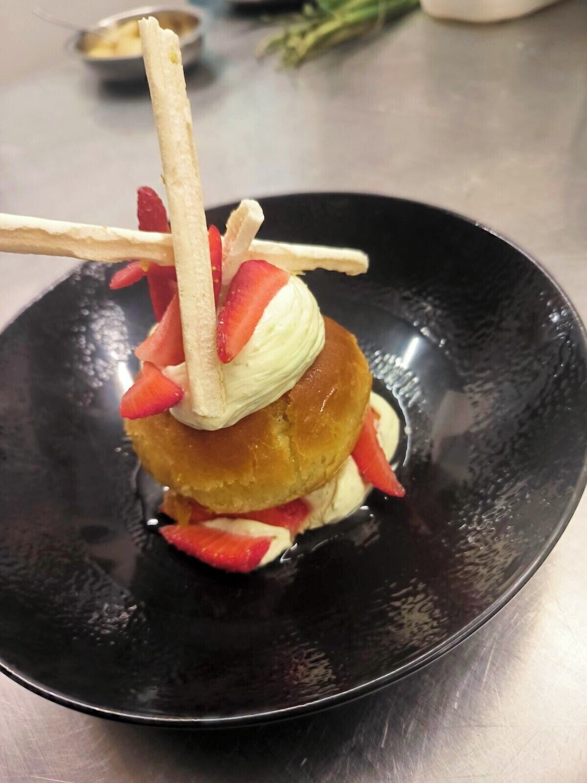 A dessert on a black plate with a pastry, strawberries, and a scoop of ice cream.