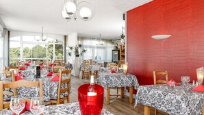 Een eetruimte met meerdere tafels, elk voorzien van tafelkleden met een patroon en rode servetten.