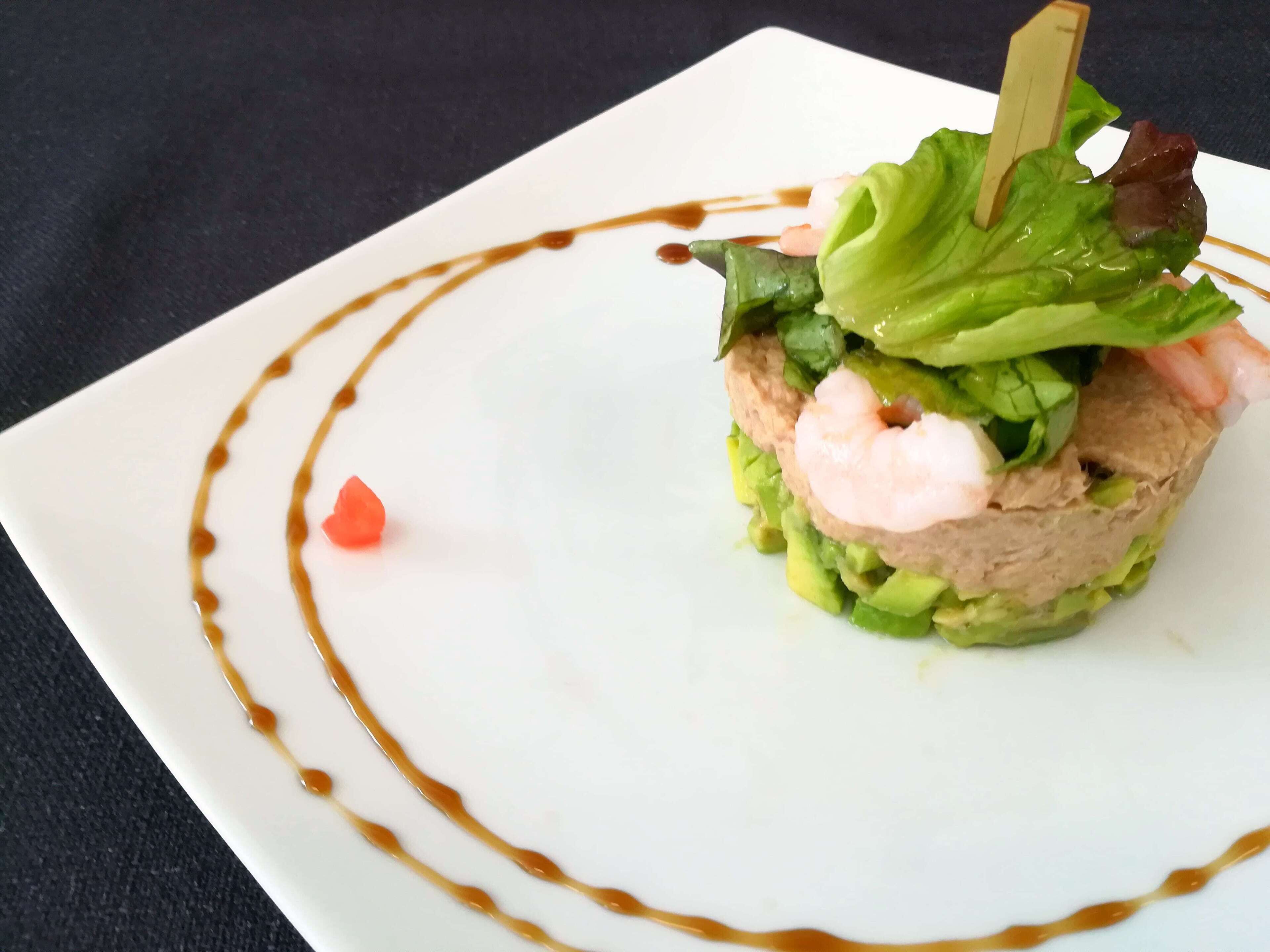 A square white plate with a seafood dish, garnished with lettuce and a toothpick, and drizzled with sauce.